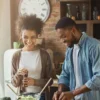 Laughing black couple preparing salad in kitchen