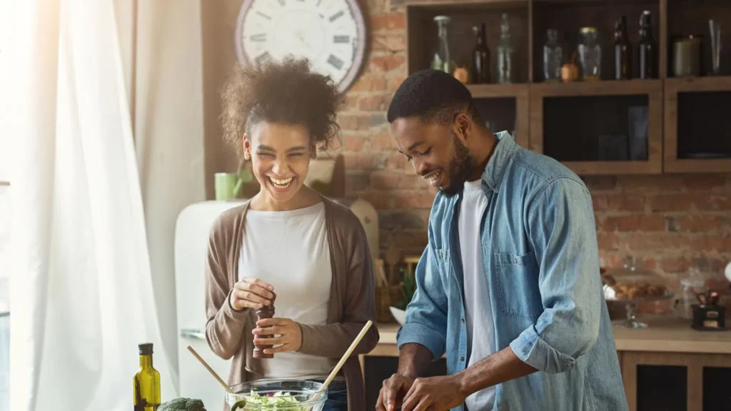 Laughing black couple preparing salad in kitchen